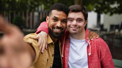Young Man With Down Syndrome And His Mentoring Friend Taking Selfie